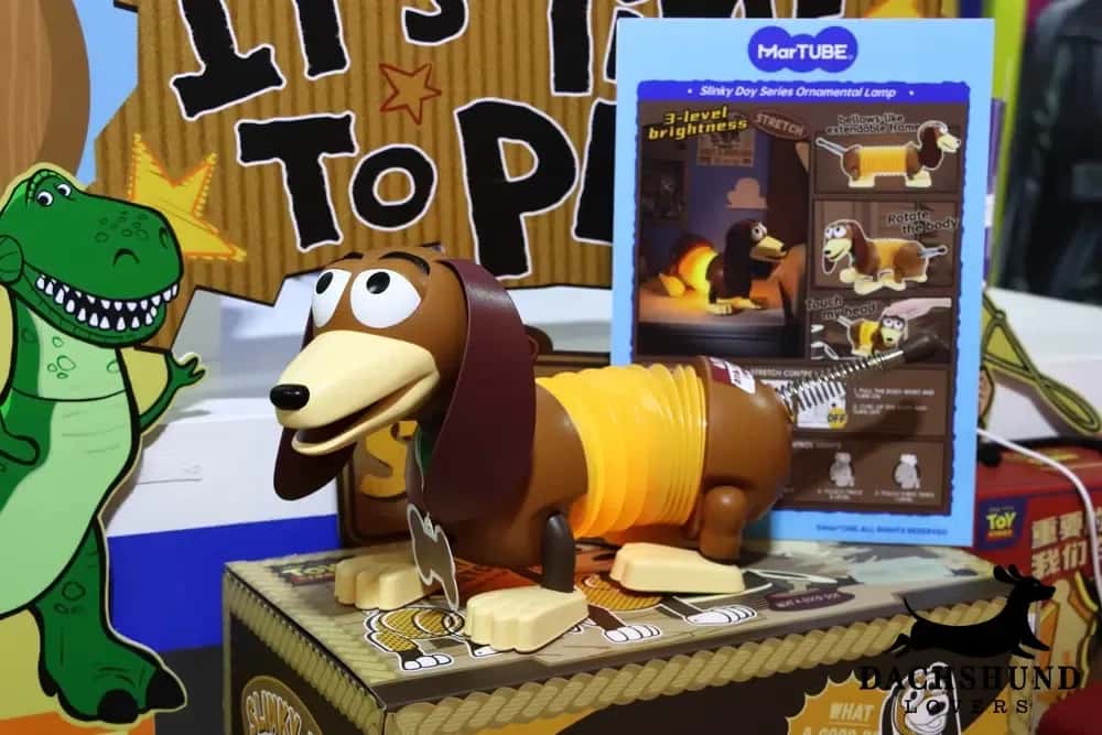 Toy-themed display featuring a Slinky Dog lamp with three brightness settings. A cartoon dinosaur stands nearby. Fun and playful atmosphere.