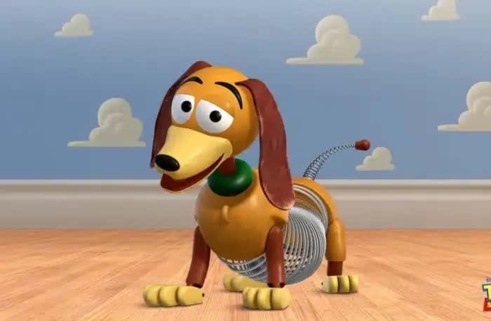 A cartoon character, Slinky Dog, with a bright smile stands on a wooden floor. It has a slinky body and a playful expression. Background features clouds on a blue wall.